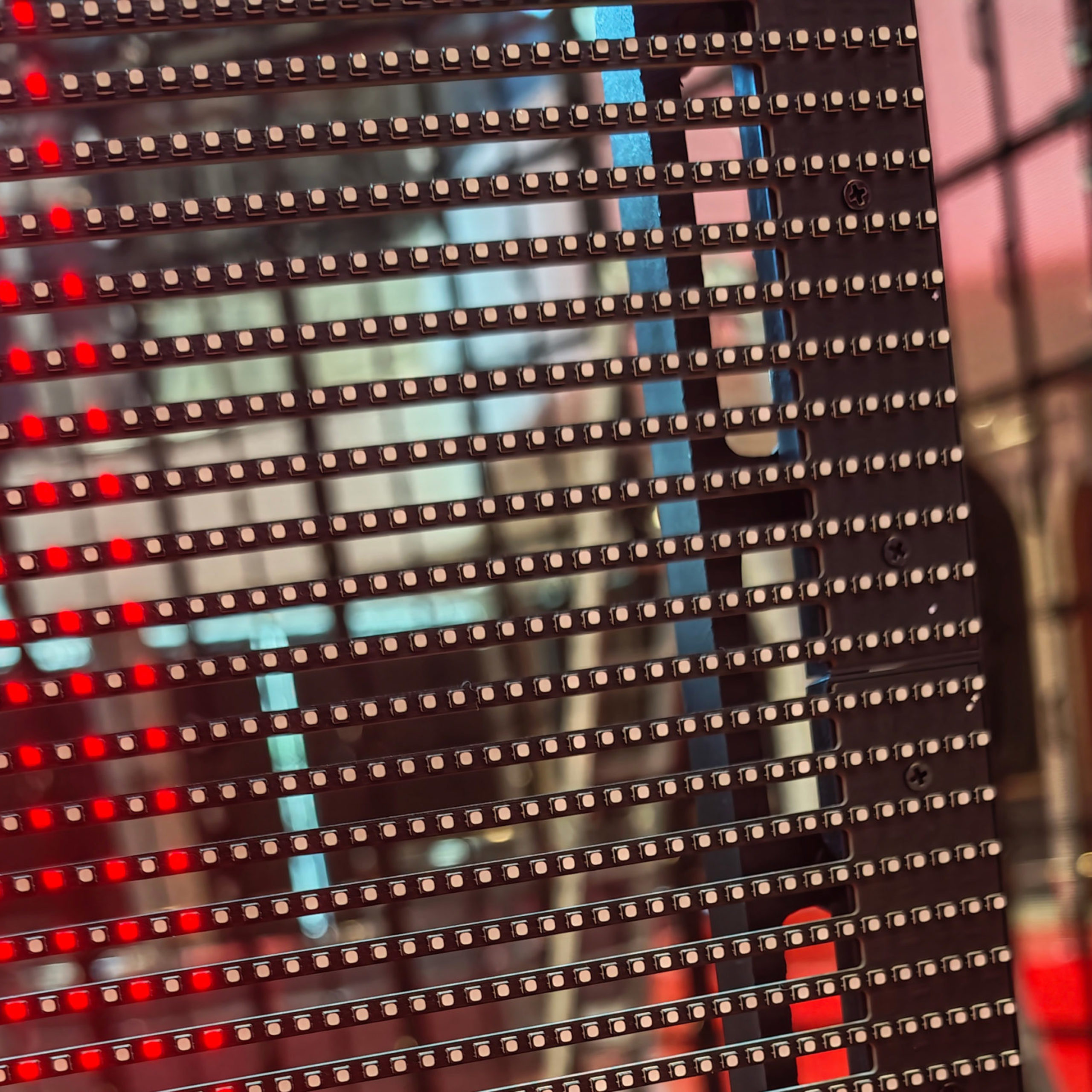 Крупный план: светодиодные линейки прозрачного LED экрана светятся красным, между ними просвечивает зал.